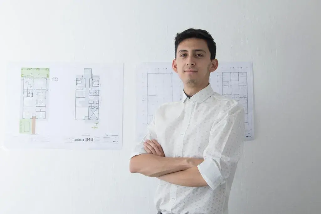 Retrato de Fernando, colaborador de InOut Arquitectura, posando frente a planos técnicos de fondo.